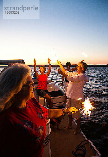 Eine Gruppe von Menschen zündet an der Vorderseite ihrer Boote ein Feuerwerk an  um einen Feiertag zu feiern  während sie in der Abenddämmerung auf einem See schwimmen.