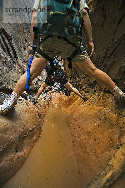 Drei Menschen zwängen sich zwischen zwei Wänden über Wasser im Slot Canyon  Utah.