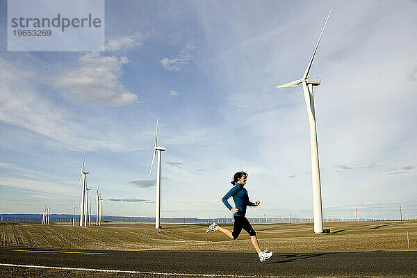 Eine Frau joggt eine Straße entlang  im Hintergrund drehen sich Windmühlen.