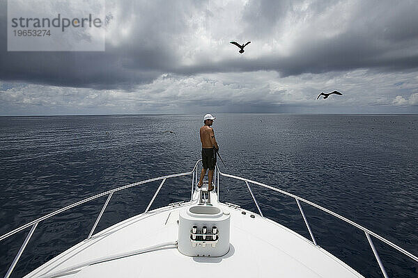 Weite Sicht auf einen Mann  der am Bug eines Bootes fischt  mit einem Vogel und dunklen Wolken über ihm in Costa Rica.