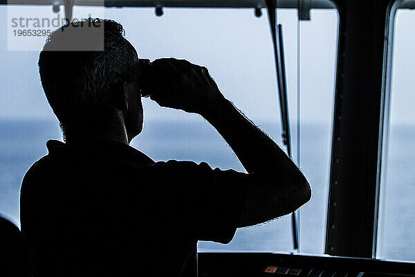 Silhouette eines Mannes mit Fernglas auf einem Containerschiff auf See