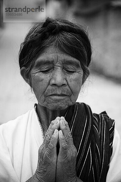 Eine ältere indigene Frau faltet zum Gebet die Hände.