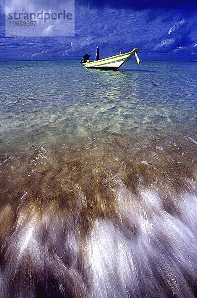 Eine Weitwinkelaufnahme eines Longtail-Bootes  im Vordergrund schlagen die Wellen am Strand  Koh Phangan.