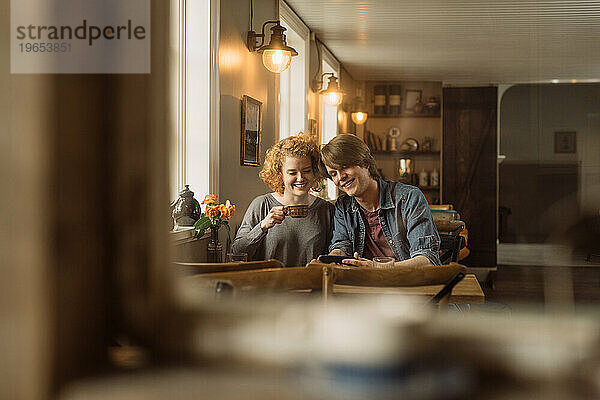 Glückliches junges Paar sitzt mit Smartphone am Tisch