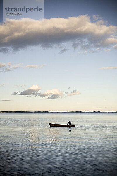 Ein Mann in einem Kanu treibt in der Abenddämmerung auf dem klaren  ruhigen  blauen Wasser entlang.