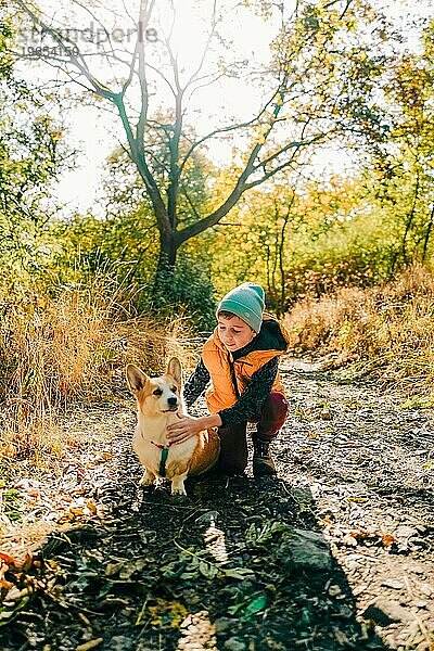 Ein Junge geht mit einem Corgi-Hund im Herbstwald spazieren