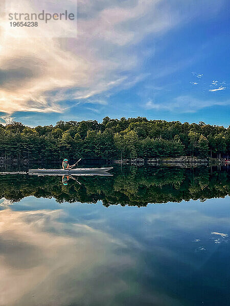 Frau paddelt an einem Sommertag allein Kajak auf einem ruhigen See.