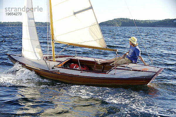 Ein fröhlicher Teenager segelt in der späten Nachmittagssonne in der Penobscot Bay in Maine mit einem wunderschönen Holzboot.