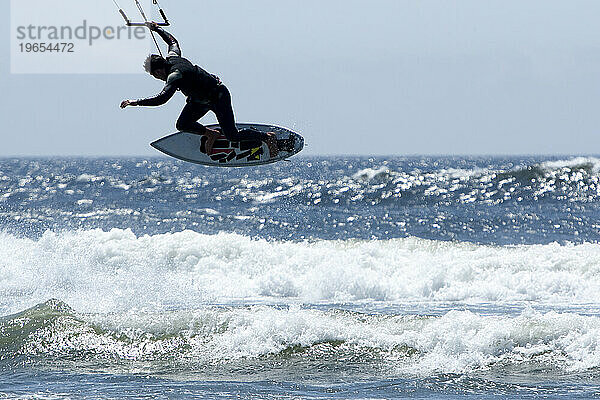 Silhouette eines männlichen Kitesurfers  der aus der Brandung springt.