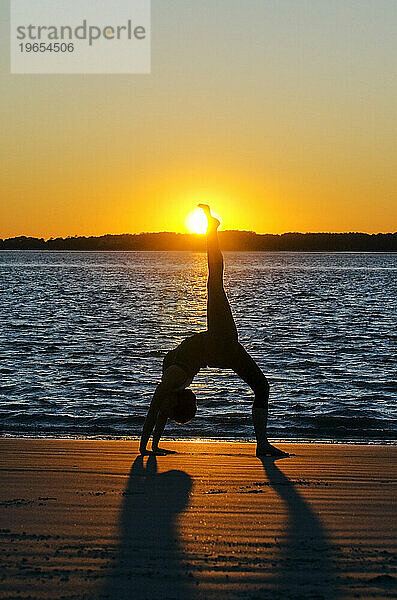 Die Silhouette einer Frau  die bei Sonnenuntergang am Strand auf Hilton Head Island  SC  Yoga macht.