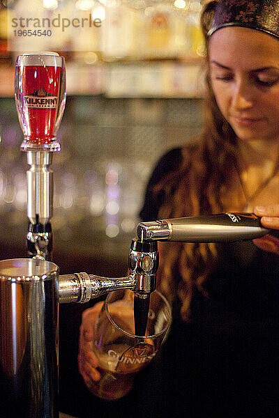 Eine Frau schenkt in einer Bar ein Bier ein.