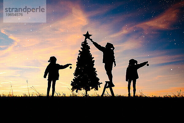 Silhouette von Kindern  die einen Weihnachtsbaum schmücken