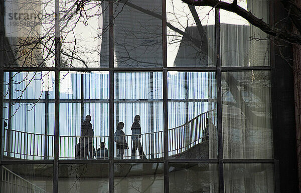 Silhouette von Menschen  die über einen glasüberdachten Gehweg gehen.