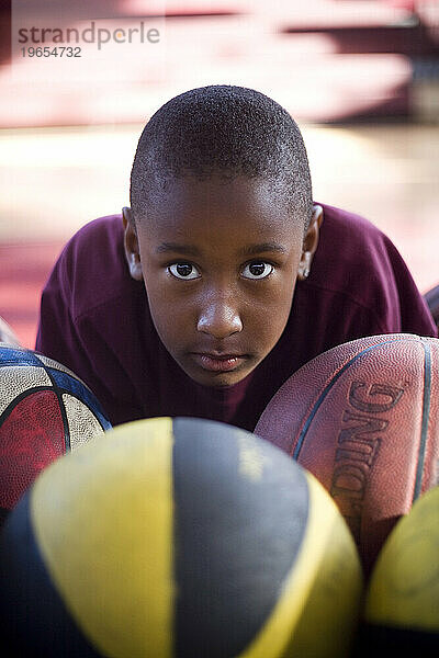 Ein kleiner Junge liegt inmitten einer Gruppe Basketbälle.