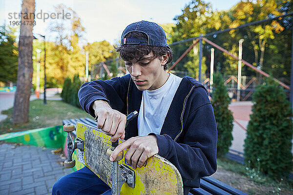 Skateboarder repariert sein Skateboard im Park