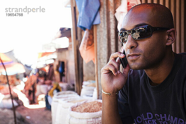 Ein junger äthiopischer Mann arbeitet an seinem Mobiltelefon  während er einen Gewürzmarkt in der äthiopischen Stadt Harar besucht.