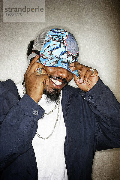 Junger afroamerikanischer Hip-Hop-Mann mit Mütze und lächelndem Handy.