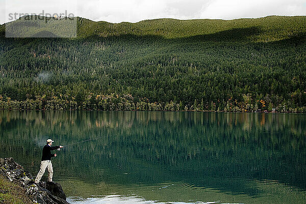 Ein Fliegenfischer warf seine Angel in den Lake Crescent. Auf der anderen Seite des Sees ist der dichte grüne Wald des Olympic-Nationalparks zu sehen.