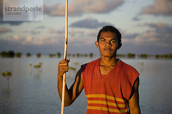 Ein Mann hält seinen Speer  während er in der Abenddämmerung in den Mangrovenbäumen fischt.