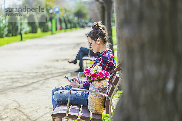 Seitenansicht einer jungen Hipster-Frau  die entspannt auf einer Parkbank sitzt