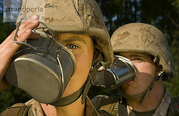 Marinerekruten trinken während einer Feldübung Suppe aus Kantinen. Jeder Marine trägt Wüstentarnuniform und Helme.