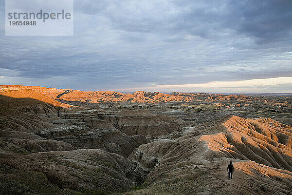 In den Badlands von South Dakota geht ein Mann einen Bergrücken entlang  während die Sonne einen alpinen Glanz über die Sandberge wirft.