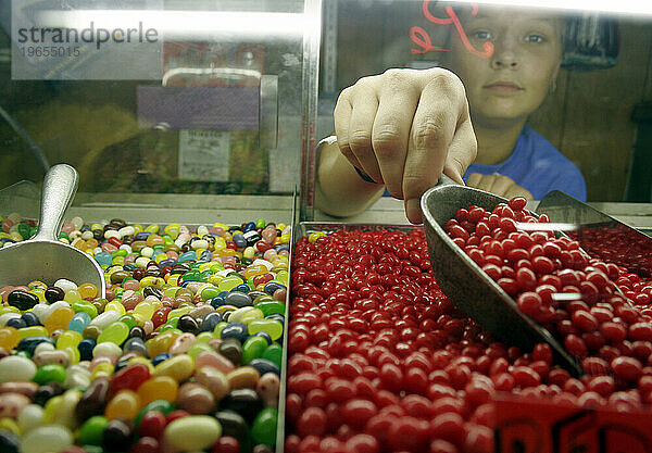 Eine junge Arbeiterin in einem Süßwarenladen schaufelt für einen Kunden rote Gummibärchen.