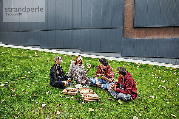 Junge Leute unterhalten sich und essen Pizza im Innenhof des Campus