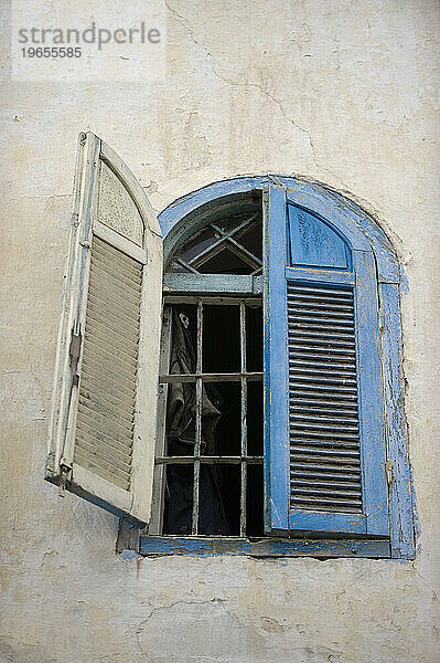 Ein verblasster blauer Fensterladen öffnet ein Fenster zur Straße.