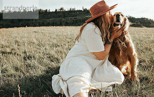 Frau im weißen Kleid küsst lächelnden Hund