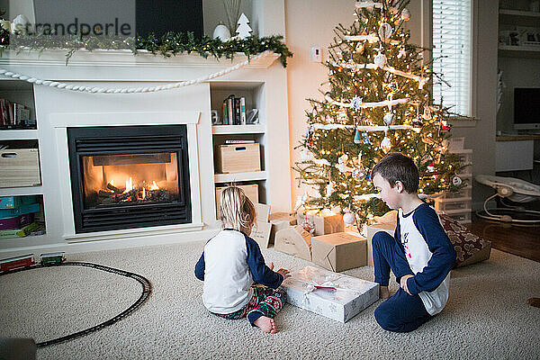 Junge und Mädchen öffnen gemeinsam Geschenke unter dem Weihnachtsbaum