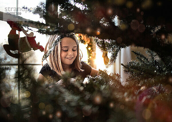 Kleines Mädchen lächelt  während es zu Weihnachten einen Kiefernbaum schmückt