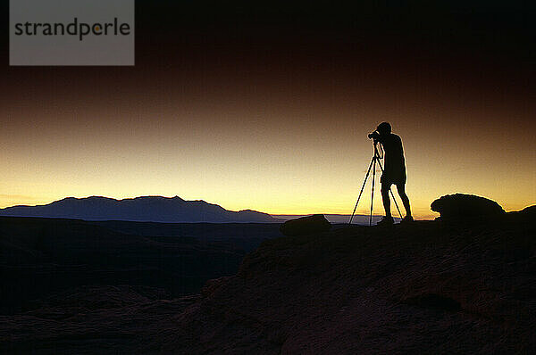 Silhouette eines Mannes und eines Stativs  die den Sonnenuntergang fotografieren.