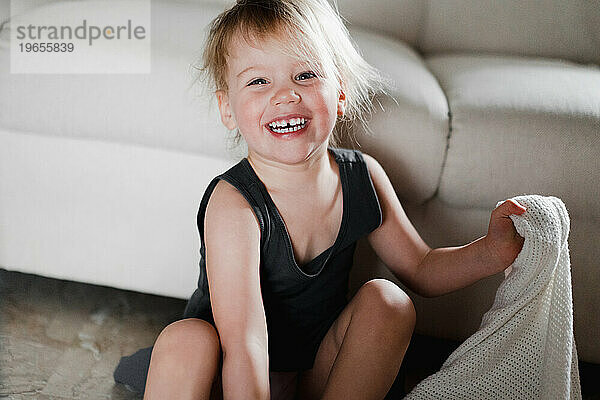 Verspieltes  zotteliges Mädchen lacht fröhlich  während es auf dem Boden sitzt