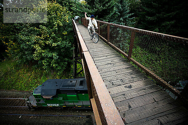 Ein Radfahrer überquert eine Brücke und gibt einem Schaffner auf den Bahngleisen unten ein Zeichen.