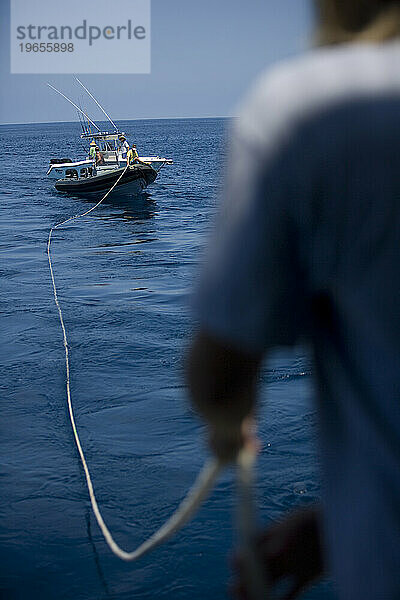 Ein Mann zieht an einem Seil  das an einem entfernten Boot befestigt ist und auf ihn zuschwebt.