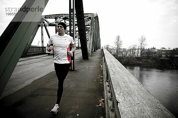 Ein Mann joggt über eine Stahlbrücke über einen Fluss.