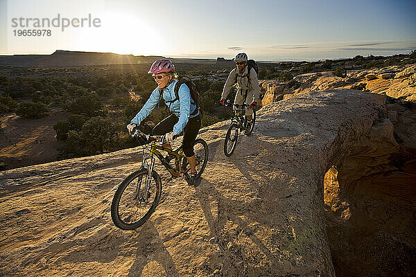 Ein Mann und eine Frau reiten über einen natürlichen Felsbogen in der Wüste in der Nähe von Moab  Utah.