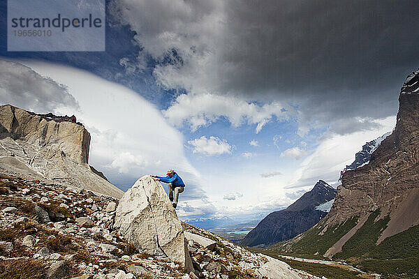 Ein Mann klettert auf einen Felsbrocken mit Blick auf ein dramatisches Tal.