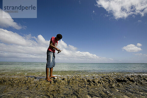 Ein junges Mädchen reinigt zwei Fische  während es auf einem Bankriff  einem freiliegenden Korallenabschnitt  steht.