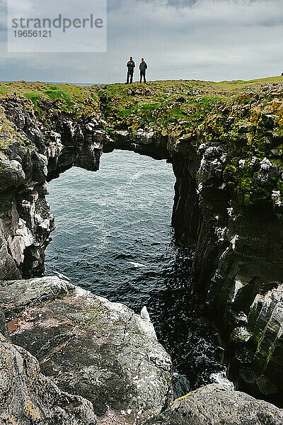 Männer wandern auf einer natürlichen Brücke über den Ozean auf einer Klippe mit grünem Gras