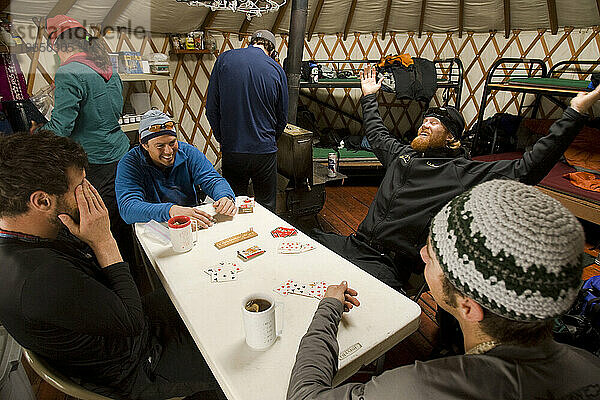 Eine Gruppe von Freunden lacht und spielt Karten in einer winterlichen Jurte im Hinterland.