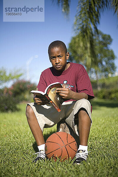 Porträt eines kleinen Jungen  der mit einem Basketball zu seinen Füßen liest.