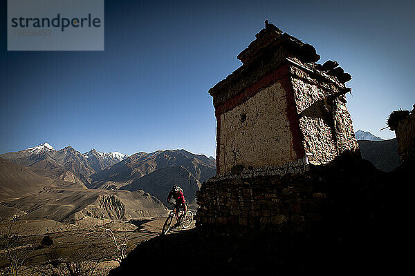 Ein Mann fährt unter blauem Himmel mit dem Mountainbike um die Ecke eines nepalesischen Gebäudes.