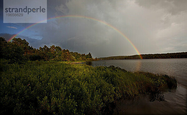 Nach einem Sommerregen bildet sich über einem See ein Regenbogen.