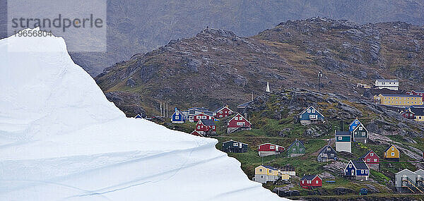 Die farbenfrohen Häuser von Ammassalik im Osten Grönlands werden von einem Eisberg im Hafen in den Schatten gestellt.