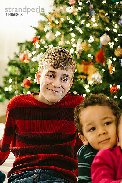 Lächelnder  glücklicher Teenager mit Geschwistern zu Weihnachten mit Lichtern und Bäumen
