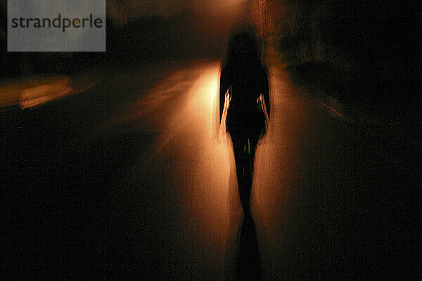 Die Silhouette einer Frau vor einer reflektierenden Straße in der Nacht.