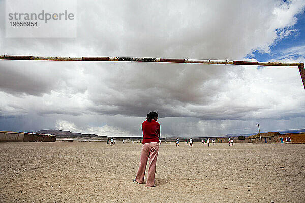 Ein Mädchen steht lässig da  während sie Torwart auf einem Fußballplatz in einer kleinen Gemeinde in der Nähe der Atacama-Wüste in Bolivien spielt.