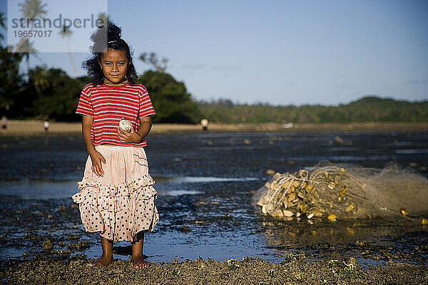 Ein rosa gekleidetes kleines Mädchen steht bei Ebbe am Riff und hält einen kleinen Fisch.